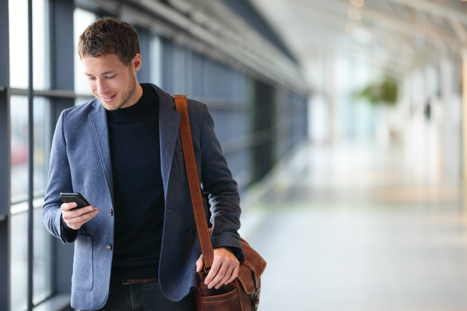 A man walking through an office corridor, looking at his phone