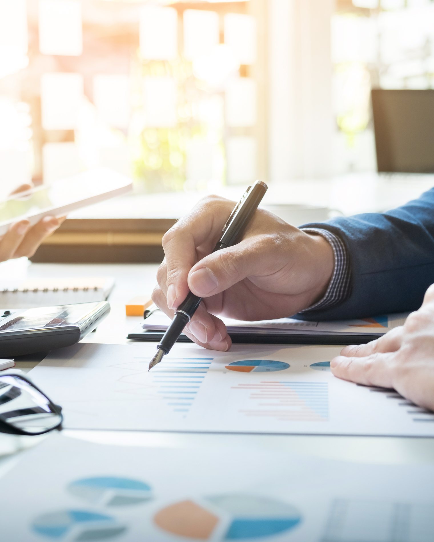 Hands with a pen and calculator reviewing printed financial reports on a desk.