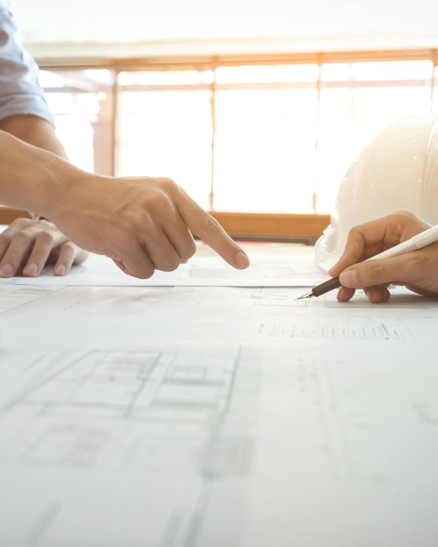 Two people’s hands pointing at and marking up a technical drawing on a desk.
