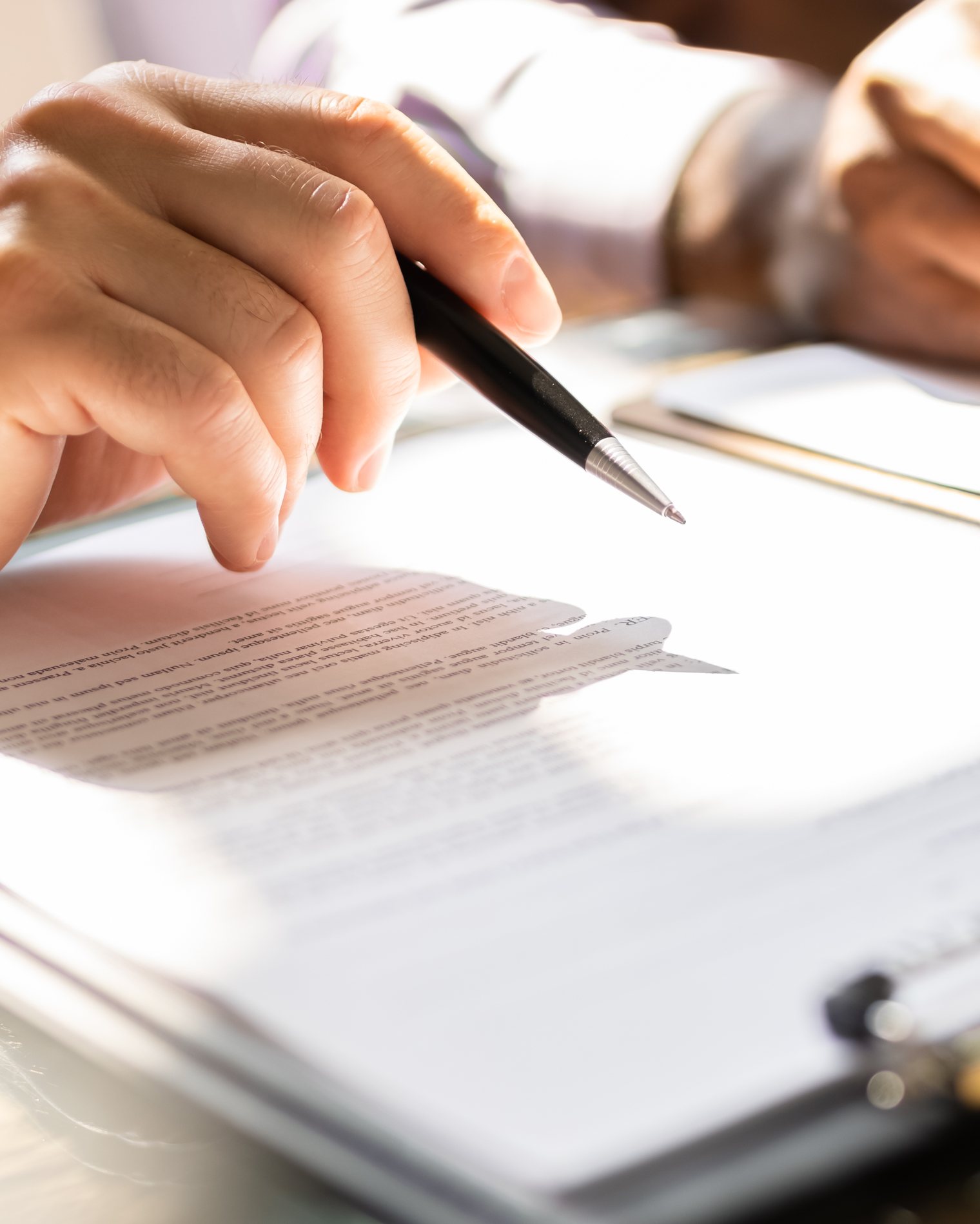 Hands holding a pen over a client agreement on a desk, beside a pair of reading glasses.
