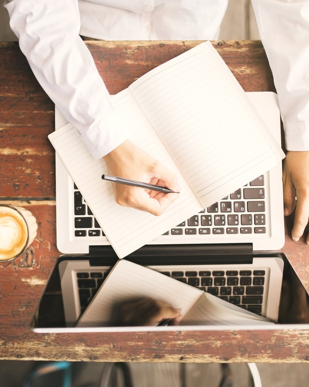 Notes being written by hand beside an open laptop on a desk